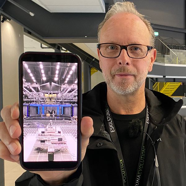 Bild på Micke Lönnberg, evenemangschef på Destination Eskilstuna. Han håller upp en mobiltelefon där han visar en bild på när scenen för Melodifestivalen byggdes i Eskilstuna.