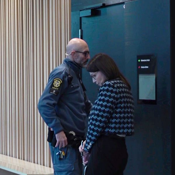 En manlig säkerhetsvakt står bredvid en kvinna i en korridor utanför en dörr in till en tingsrättssal.