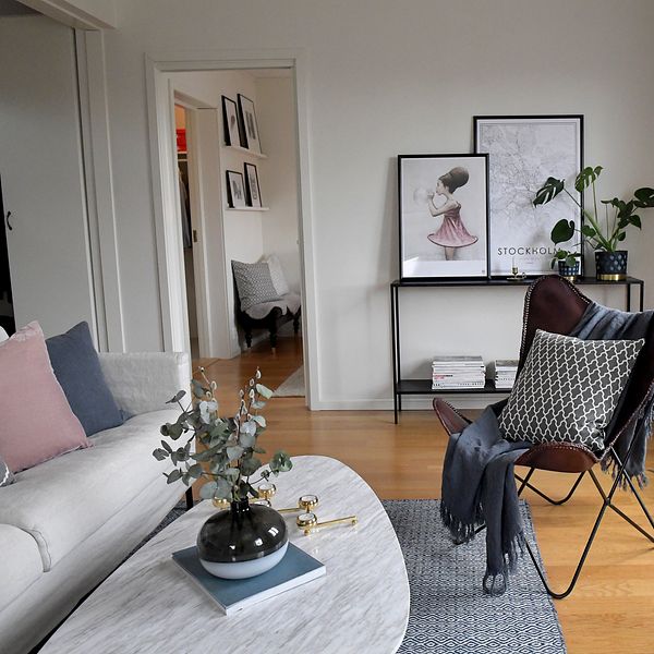 Modernt inredd vardagsrum med soffa, fåtölj och dekorationer på bord och hylla.