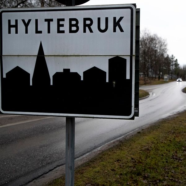 Vägskylt vid infart till Hyltebruk, omgivning med väg och träd.