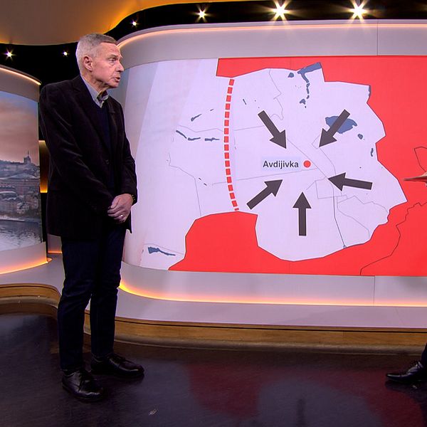 Två män står i studio på varsin sida om en karta med pilar.