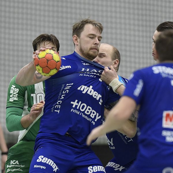En handbollsmatch där spelare i blå och gröna tröjor kämpar om bollen. Fokuserade ansikten tillhör spelare i intensiva positioner medan de försöker ta kontroll över spelet.