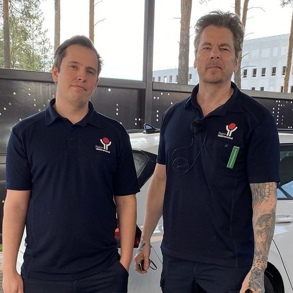 Två personer i arbetskläder står bredvid en bil med logotypen ”Region Västmanland”.