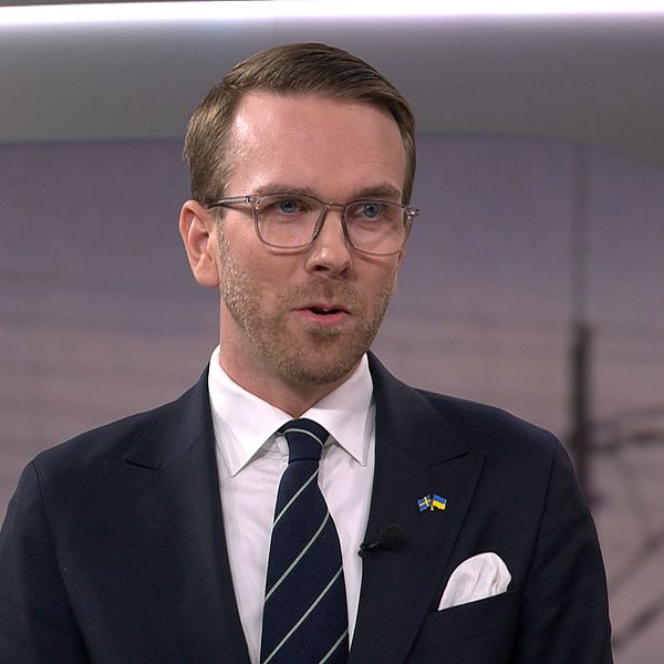 Man i kostym och glasögon står i en tv-studio.