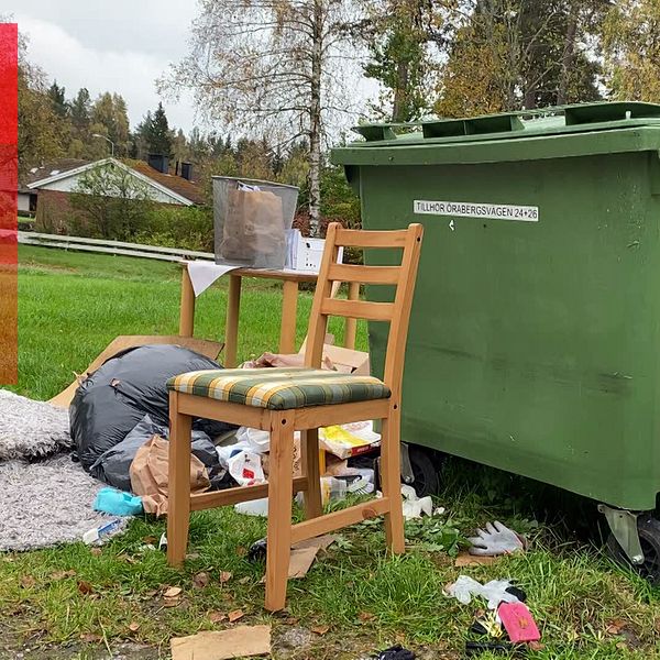 Gamla möbler och tyger ligger slängda framför en grön container.