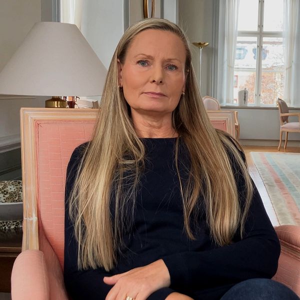 En kvinna i långt ljust hår, Ulrika Gustafsson Lindberg, sitter i en rosa fåtölj i en stor sal.