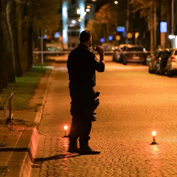 polis står på en avspärrad gata och lyser med en ficklampa