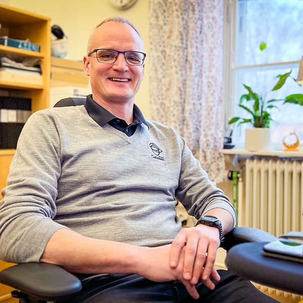 En glad man i grå tröja sitter vid sitt skrivbord