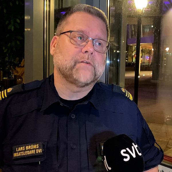 Person i polisuniform med namnskylt ”Lars Broms”, hastighetspolis, som håller en mikrofon med SVT-logotyp. Bakgrunden visar en nattlig stadsmiljö med oskarpa ljus och fönster.