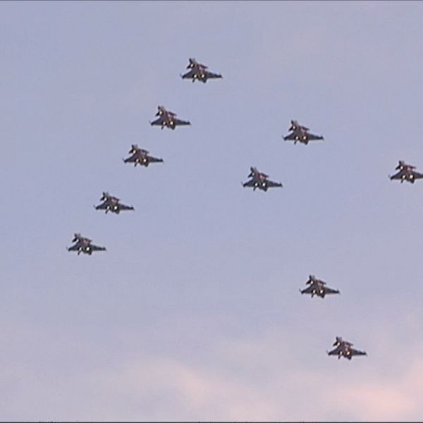 Flera stridsflygplan flyger i formation på en klar himmel, arrangerade i en synlig V-form.