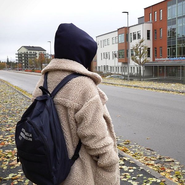 En elev med ryggsäck och huvan uppe står utanför Internationella engelska skolan i Växjö