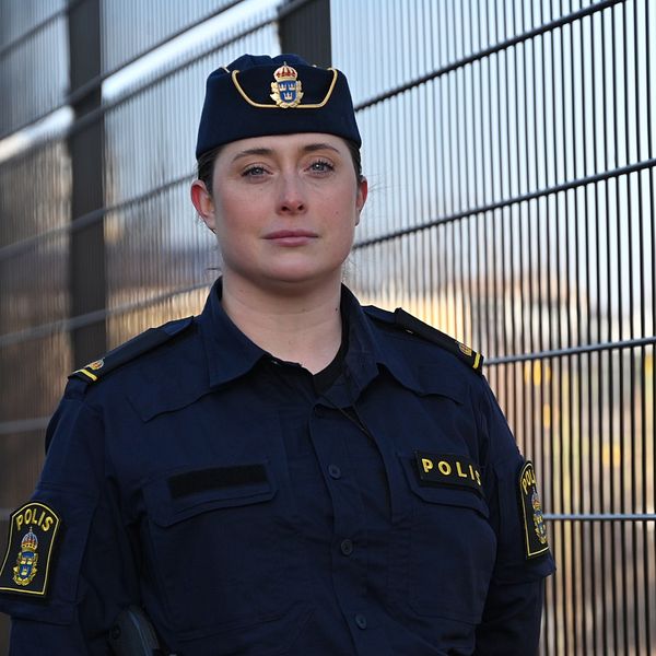 Polisklädd person står vid ett metallstaket utomhus.