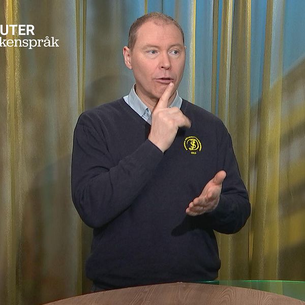Patrik Drivstedt står i en studio och tecknar ordet döv.