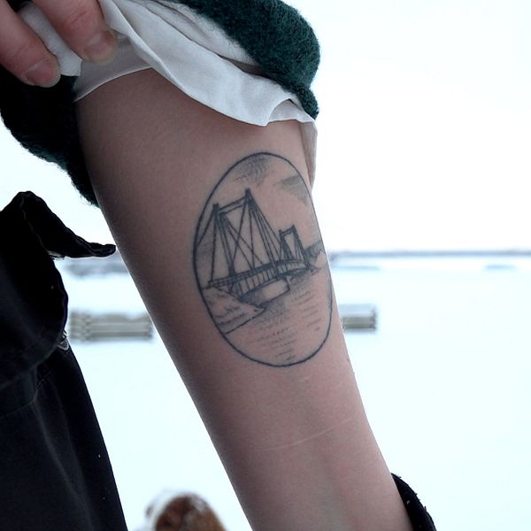 En taturerad underarm med Strömsundsbron som motiv. I bakgrunden syns den fysiska bron.