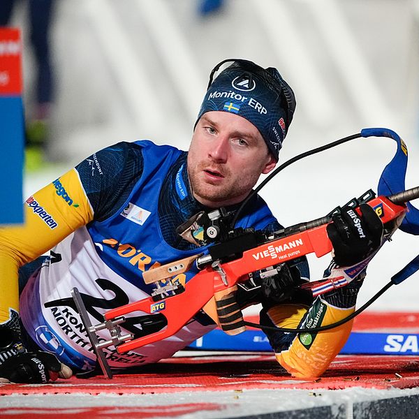 Skidskytten Jesper Nelin liggandes på skjutvallen under tävling iförd blågul dräkt, med bössan i handen,