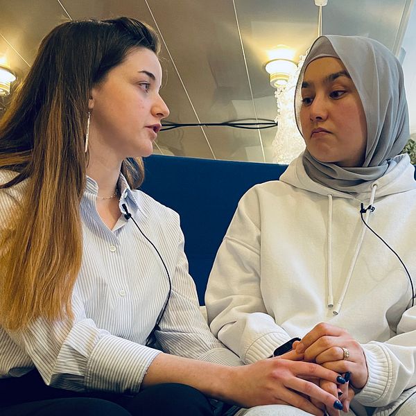 Två elever på Risbergska håller varandras händer och sitter på en blå soffa.