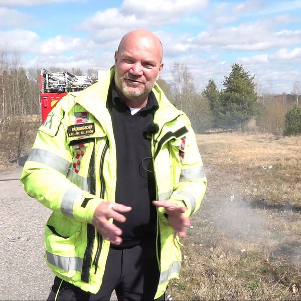 Brandman släcker mindre gräsbrand nära väg, brandbil i bakgrunden.