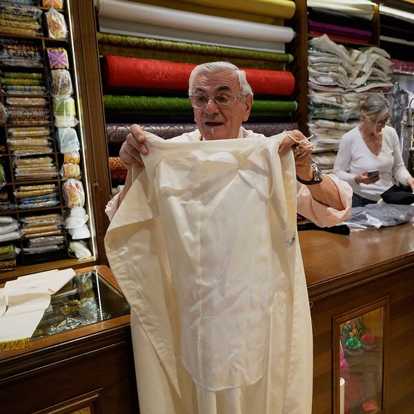 Person inspekterar tyg i en butik med hyllor fyllda av färgglada textilrullar.