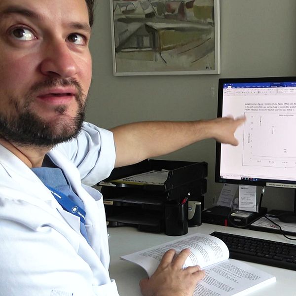 Överläkaren Ioannis Katsoularis pekar på en datorskärm som visar en graf. I handen håller han en bok.