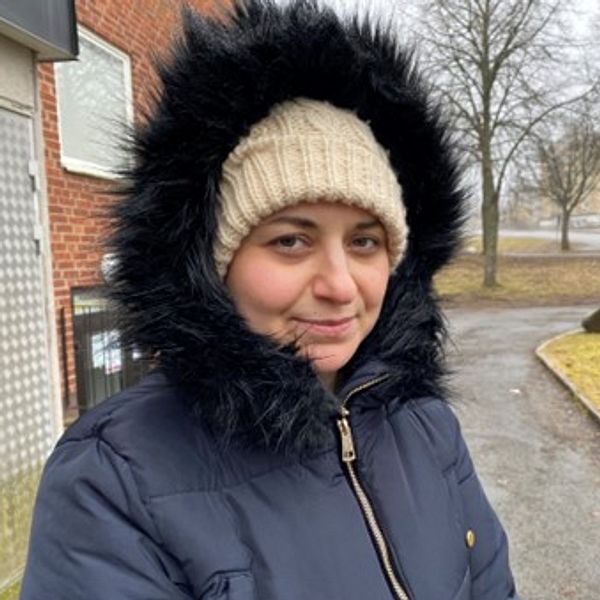 Kvinna med mössa och luva utanför hyreshus i Nässjö där två män hittades döda