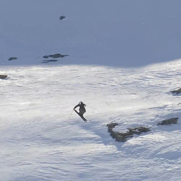 Ensam skidåkare åker nerför en snötäckt bergssida med klippor och skuggor.