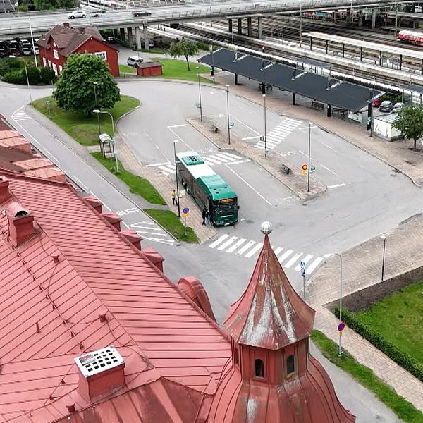 Busstation i Älmhult med en grön buss och flera perronger intill äldre byggnader och tågräls.