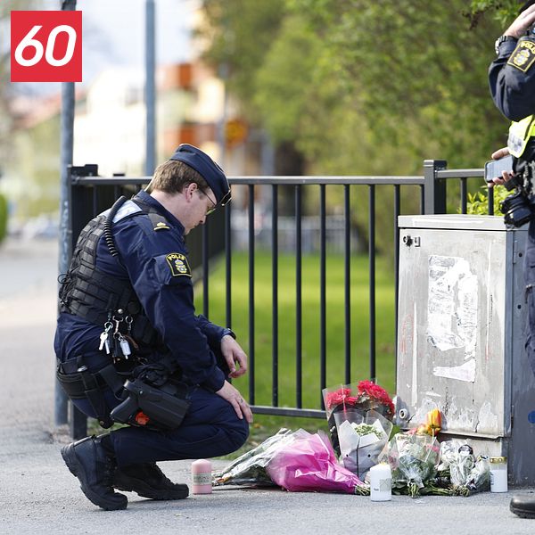 Två poliser vid ett blomhav på trottoaren, minnesplats efter händelse utomhus.