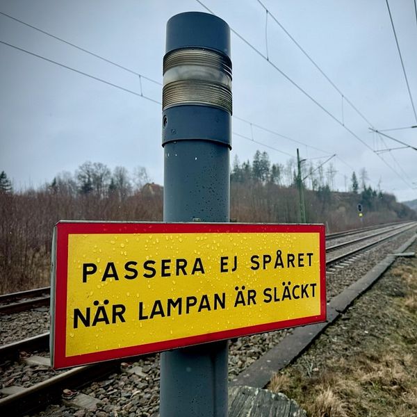 Varningsskylt vid järnvägsspår med text ”Passera ej spåret när lampan är släckt”.