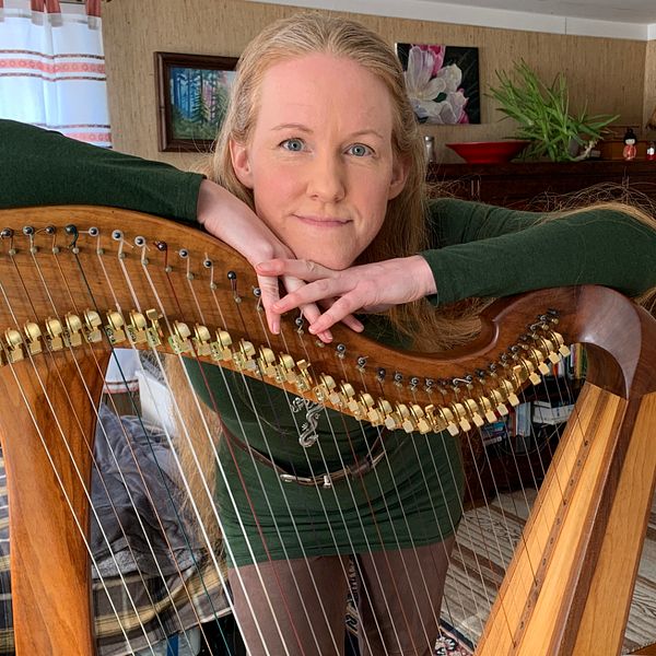 Mia Westlund står lutad över sin harpa