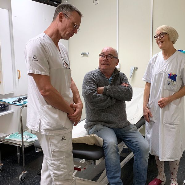 Tre personer, en läkare, en sjuksköterska och en patient står och snackar i ett besöksrum.