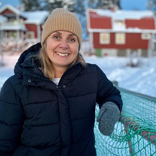 Kvinna med vinterkläder lutar sig mot ett hockeymål på en isbana.