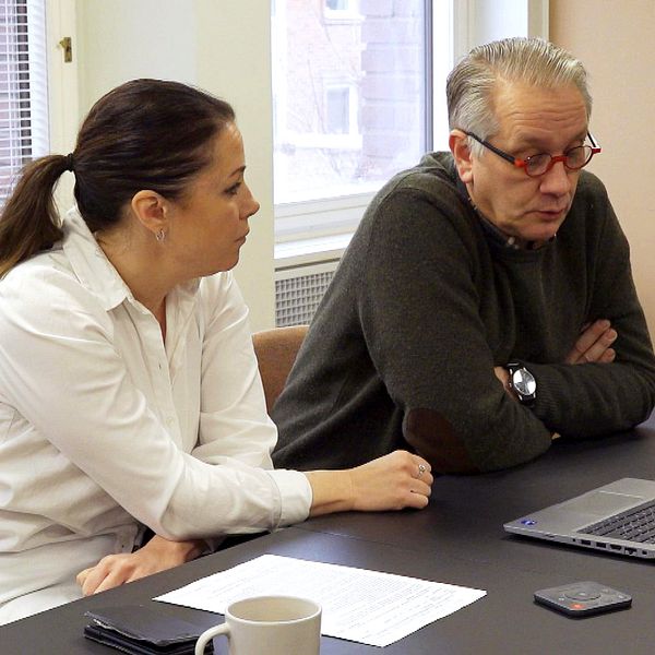 Två personer diskuterar vid ett bord med en laptop och dokument.