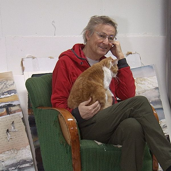 Lars Lerin sitter i en fåtölj i sin ateljé med sin katt i knäet