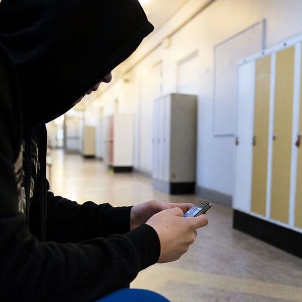 En anonym tonåring håller på med mobilen i en skolkorridor.