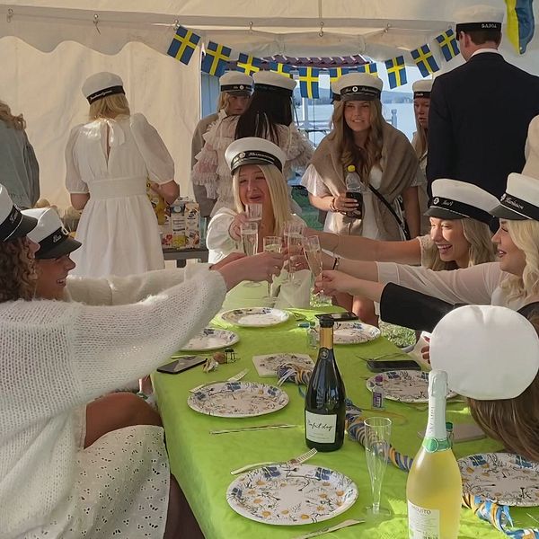 Studenter med studentmössor skålar i champagne och äter frukost