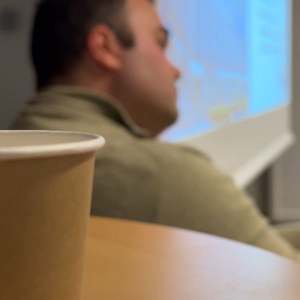 En kaffemuggi  förgrunden och en man som tittar åt sidan i bakgrunden