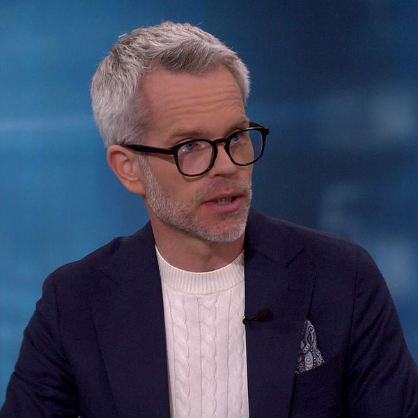Alexander Norén i kostym sitter i en tv-studio med blå bakgrund och ljus skjorta.