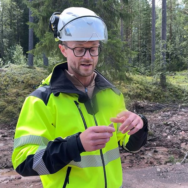 man i varselkläder och bygghjälm står och pekar på en vass sten