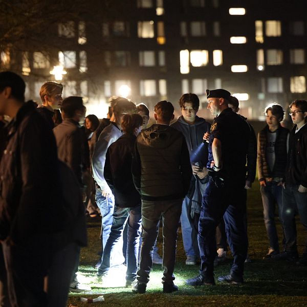 En polis står med ficklampa vid en stor grupp ungdomar på Hoppbacken i Enskede under valborgsnatten.