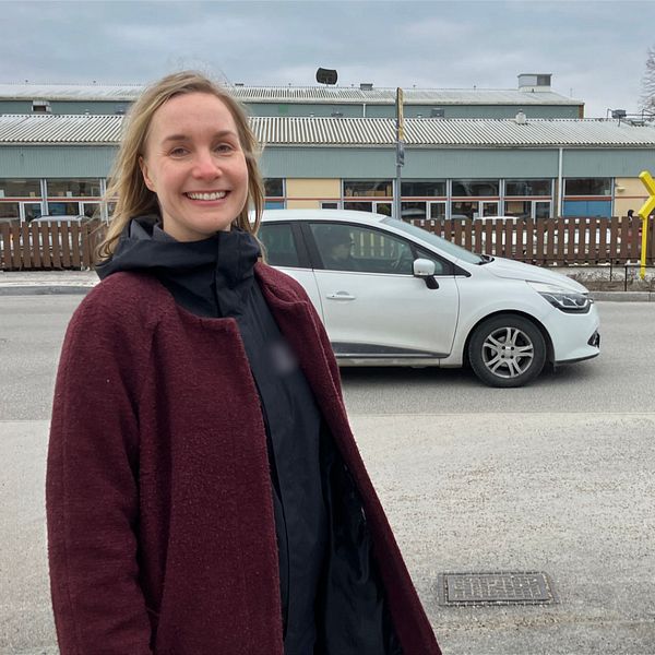 Petra Ahlman står vid väg med korsande vit bil och skolbyggnad i bakgrunden.