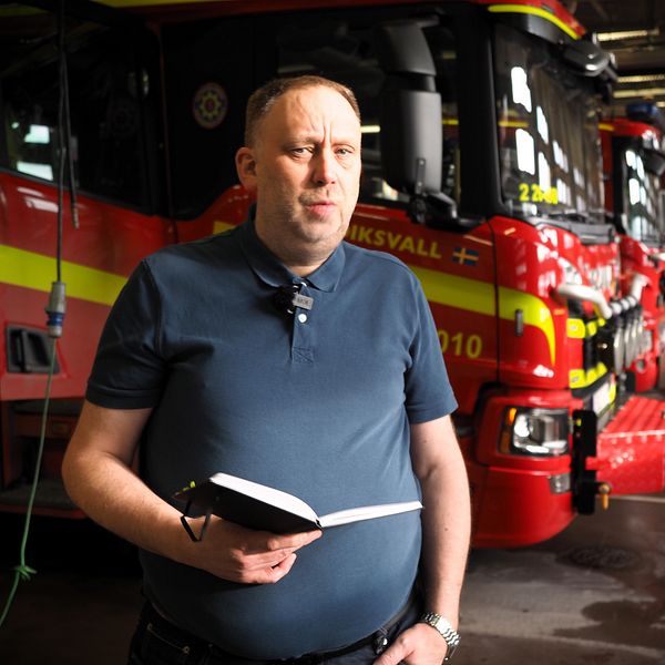 Per Svensson (S) står med anteckningsbok framför brandbilar i en brandstation.
