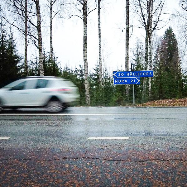 En bil åker snabbt förbi i Stadra. En skylt med Hällefors åt ena hållet och Nora åt andra.