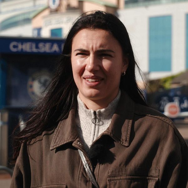 Två personer samtalar utanför Chelseas stadion Stamford Bridge i soligt väder.