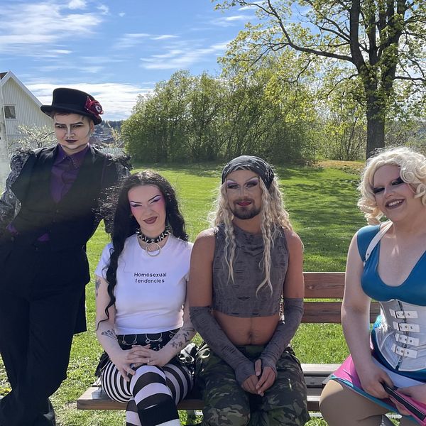Fyra personer med alternativa klädstilar sitter utomhus på en bänk i en park.