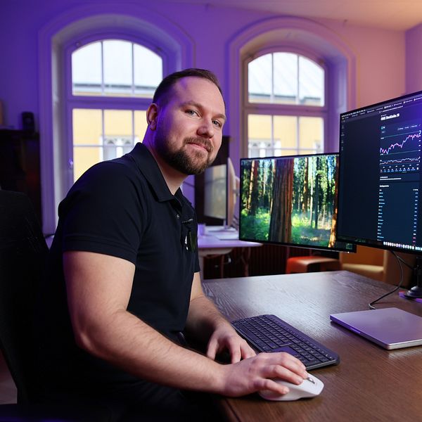 Person vid skrivbord med flera datorskärmar som visar grafer och data.