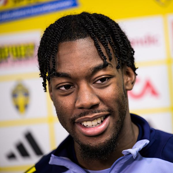 Person i sporttröja framför sponsormärkesvägg.