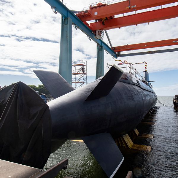 ubåten HMS Gotland under konstruktion vid kaj med stora lyftkranar i bakgrunden.