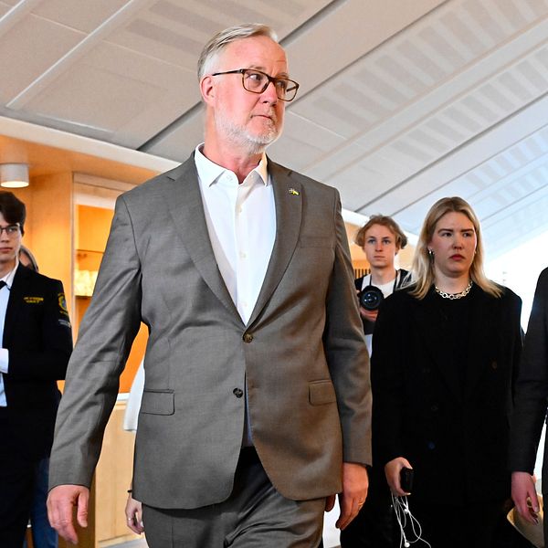 En grupp personer i kostym och kavaj går i en korridor, ser allvarliga ut.