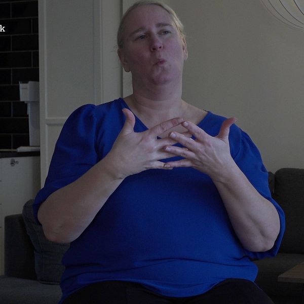 Mona Riis i blå tröja sitter i ett vardagsrum och tecknar ordet blå.