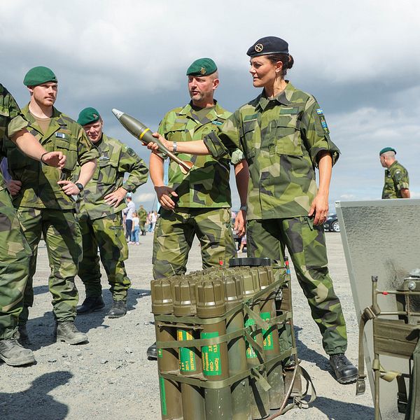 Kronprinsessan Victoria, iklädd uniform, räcker över en artillerigranat till en uniformerad militär.